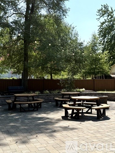 A patio with picnic tables and benches under trees.
