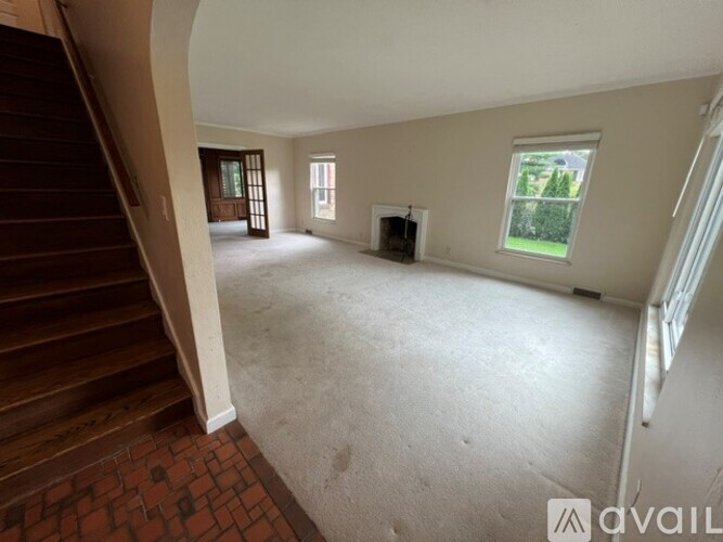 A spacious living room with a staircase on the left and a window on the right.