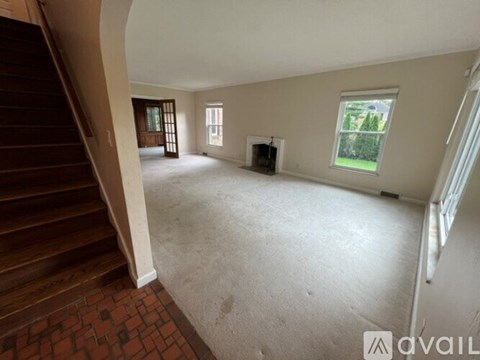 A spacious living room with a staircase on the left and a window on the right.