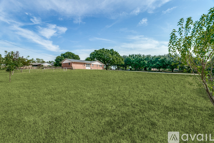A grassy field with a house and trees in the distance.