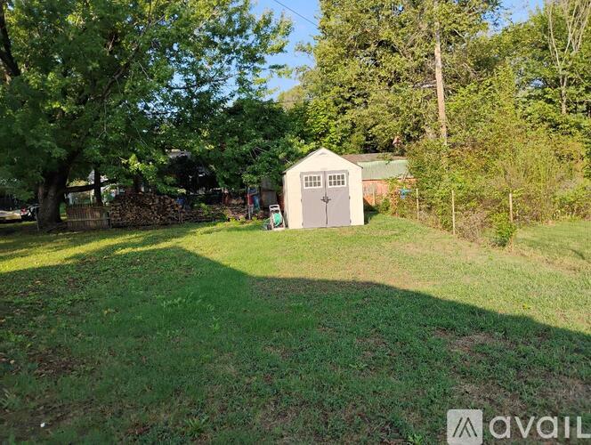 A shed sits in a grassy area with trees in the background.