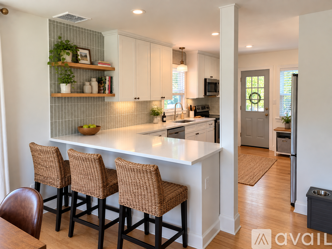 A kitchen with white cabinets and a bar area with brown chairs.