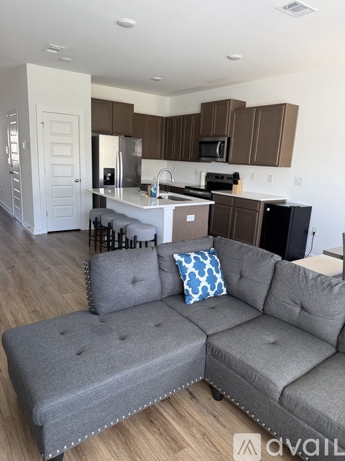 A grey couch with a blue pillow is in the middle of a kitchen and living room.