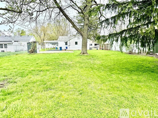A grassy field with a tree and a building in the background.