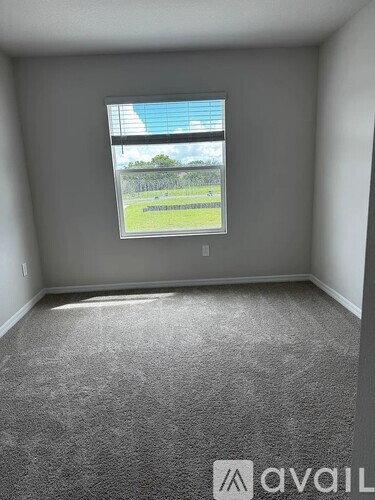 A room with a carpeted floor and a window showing a view of a pool and a fence.