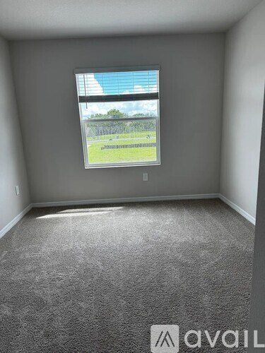 A room with a carpeted floor and a window showing a view of a pool and a fence.