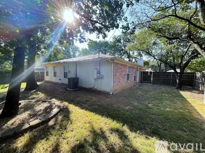 A house with a white exterior and a brown roof is surrounded by trees and has a fence.