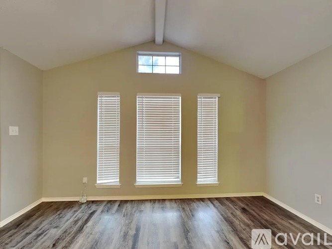 A room with wooden flooring and three windows with blinds.