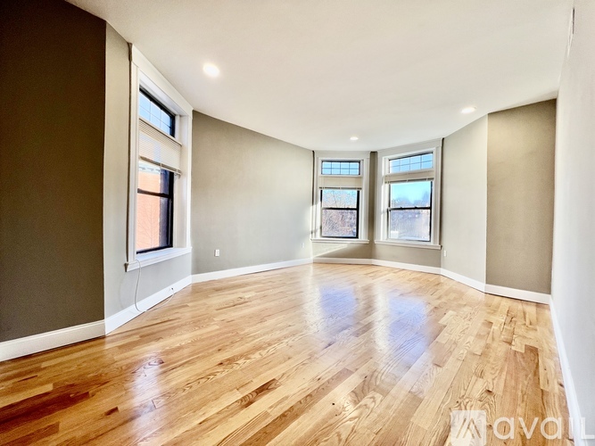 A spacious room with wooden flooring and three windows.