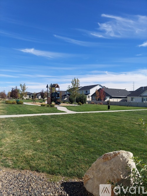 A grassy area with a large rock in the foreground and houses in the background.