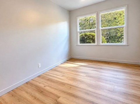 A room with wooden flooring and a window showing greenery outside.