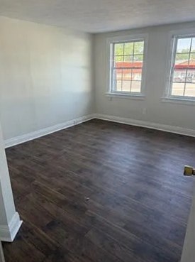 A room with wooden flooring and two windows.