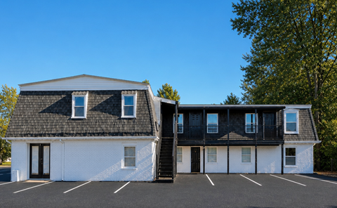 A white building with black trim and a black roof with a parking lot in front.