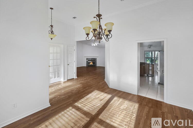 A large, empty room with a chandelier and hardwood floors.