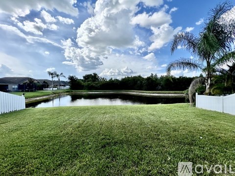 A grassy field with a pond and trees in the distance.
