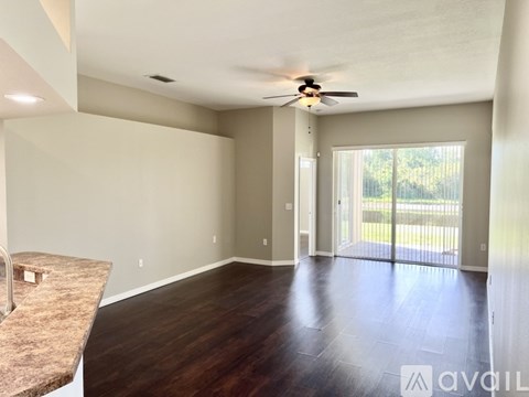 A spacious room with a ceiling fan and sliding glass doors leading to a balcony.