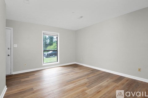 A room with wooden flooring and a window showing a view of trees and a car.