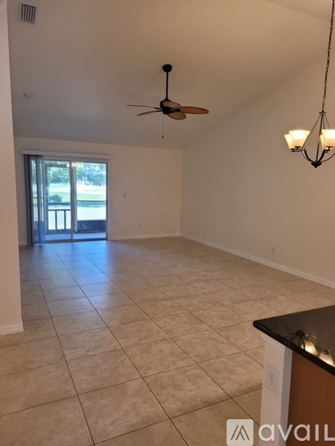 A spacious room with a ceiling fan and a sliding glass door leading to a balcony.
