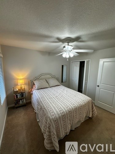 A bedroom with a bed, a ceiling fan, and a lamp on a side table.