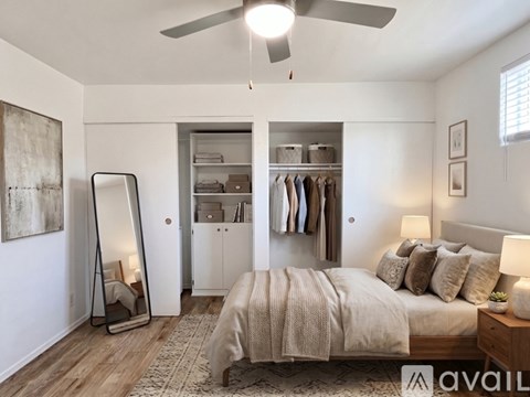 A bedroom with a large bed, a mirror, a ceiling fan, and a wardrobe.