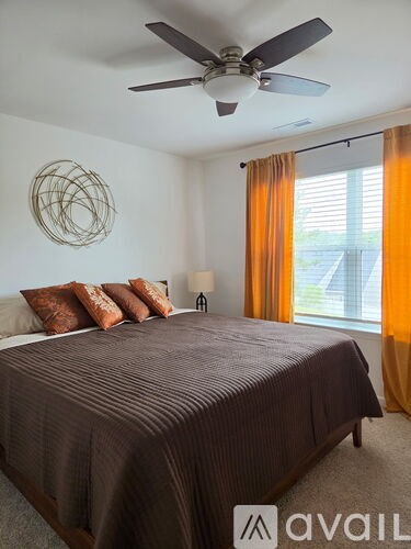 A bedroom with a bed, a ceiling fan, and a window with orange curtains.