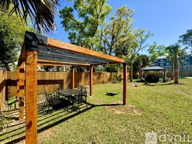 A wooden pergola with a black roof is situated in a grassy backyard.
