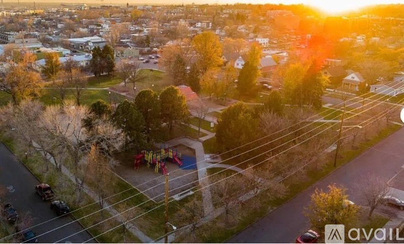 A sunset view of a neighborhood with a playground and parked cars.