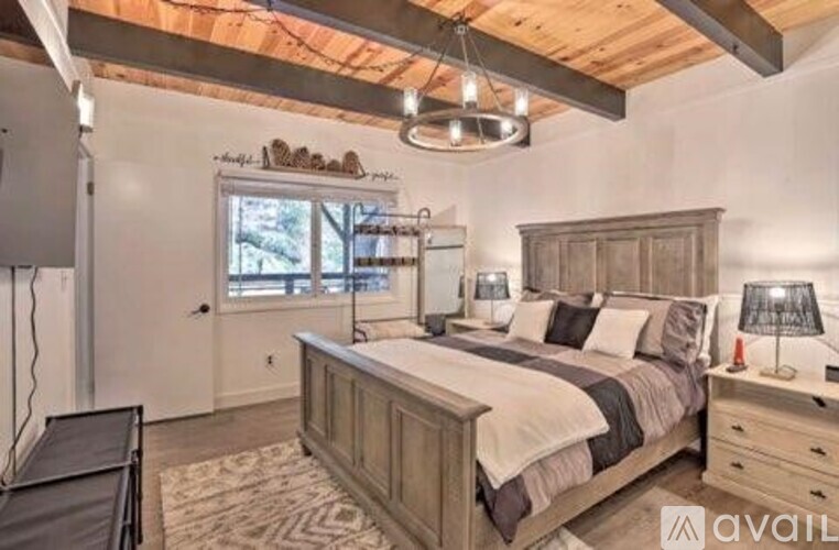 A bedroom with a large bed, a window, and a wooden ceiling.