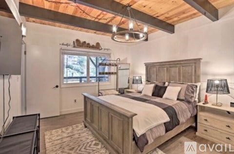 A bedroom with a large bed, a window, and a wooden ceiling.