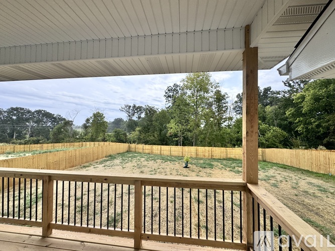 A wooden deck with a white railing overlooks a sandy area with trees in the background.