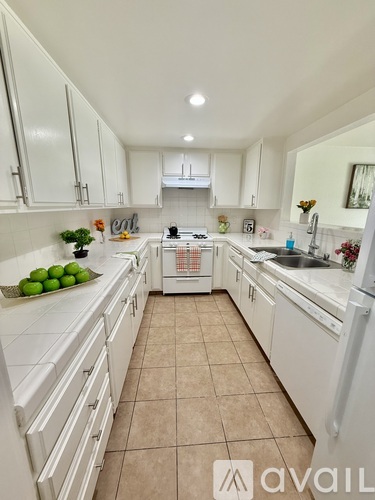 A kitchen with white cabinets and appliances, a sink, and a counter with fruit on it.