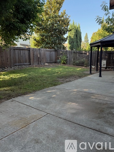 A backyard with a concrete walkway and a black awning.