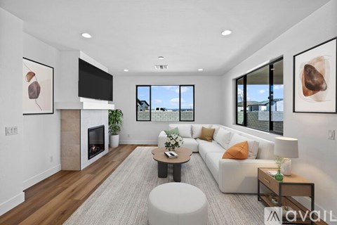 A modern living room with a white sofa, a grey rug, and a fireplace.