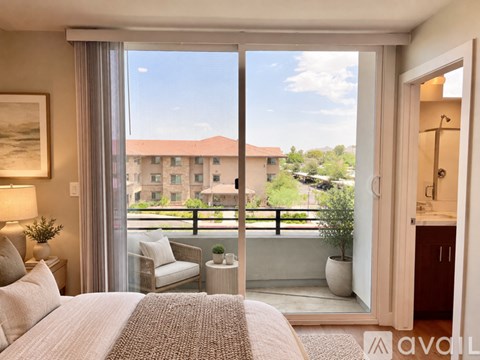 A bedroom with a large bed and a view of a balcony with a chair and a potted plant.
