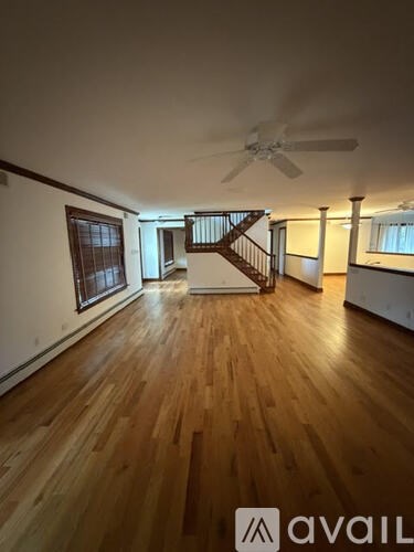 A spacious room with wooden floors and a staircase in the background.