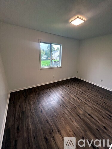 A room with wooden flooring and a window showing a view of a building and trees outside.