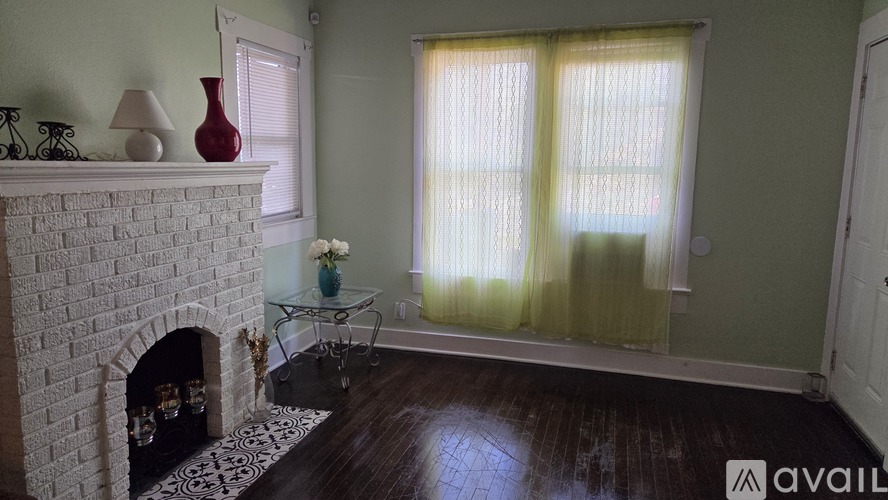 A living room with a fireplace, a glass coffee table, and a window with curtains.