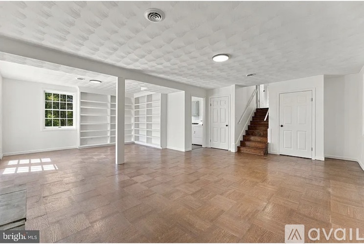 A spacious room with wooden flooring and white walls.