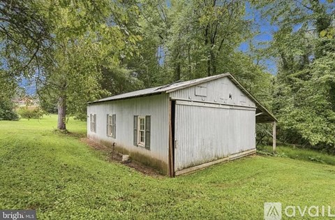 A small, old, metal building sits in a grassy field.