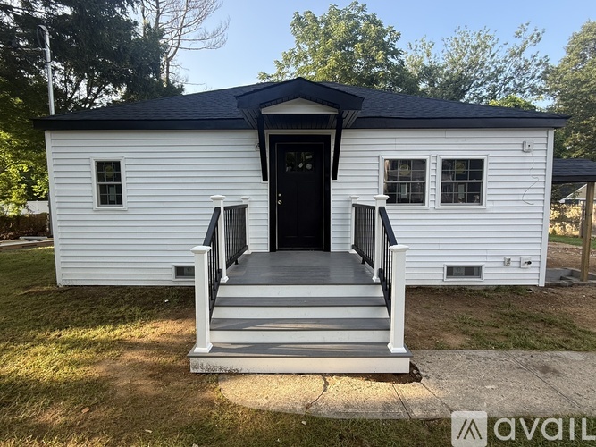 A small white house with a black door and windows is for sale.