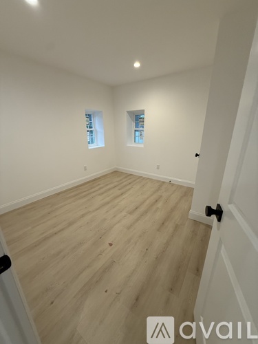 A room with wooden flooring and white walls, with two windows and a door.