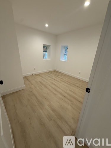 A room with wooden flooring and two windows.
