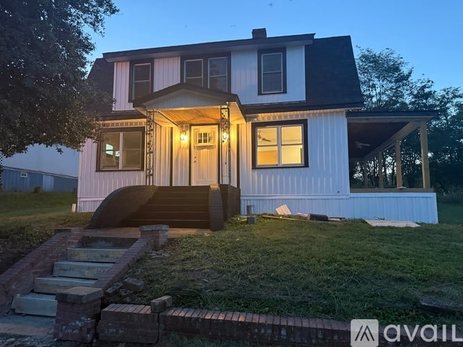 A house with a porch and a covered patio is lit up at dusk.
