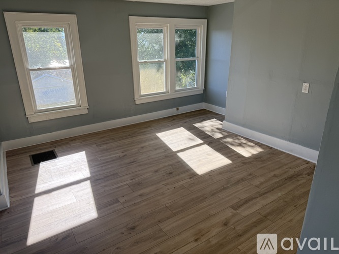 A room with wooden flooring and two windows.