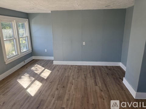 A room with wooden flooring and a window letting in sunlight.