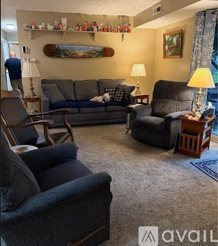 A living room with a grey couch, a black chair, and a wooden table with a lamp on it.