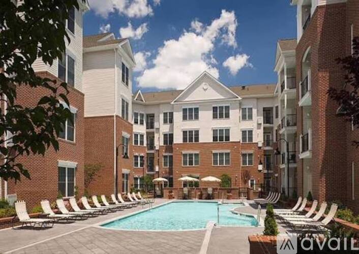 A large pool surrounded by lounge chairs and umbrellas in front of a brick building.