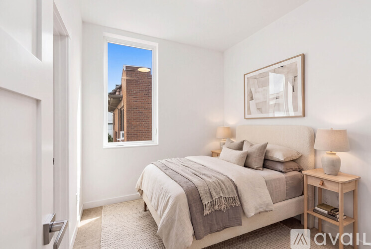 A bedroom with a bed, nightstand, and a window overlooking a brick building.