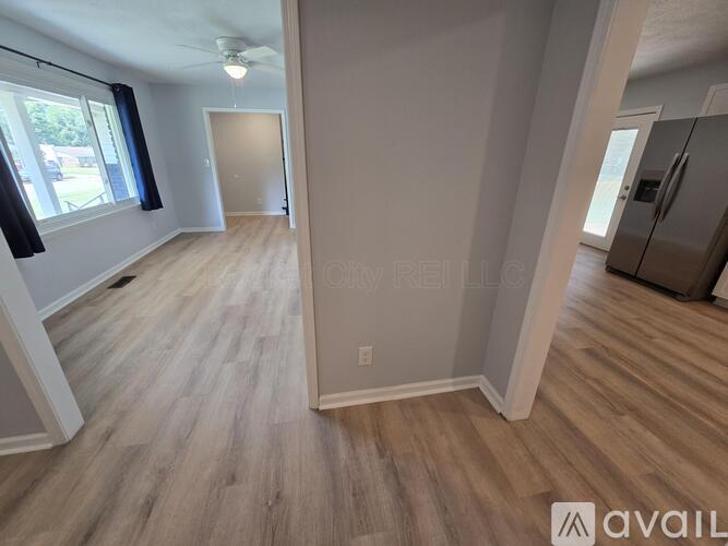 A spacious room with wooden flooring and a refrigerator in the corner.