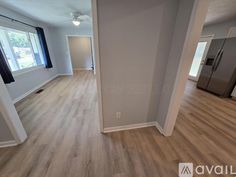 A spacious room with wooden flooring and a refrigerator in the corner.
